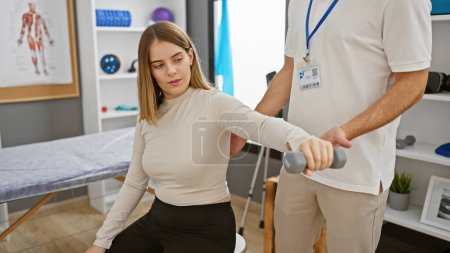 Eine Patientin führt in einer Reha-Klinik mit Unterstützung eines männlichen Physiotherapeuten Armübungen mit einer Hantel durch.