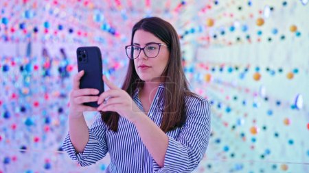 Foto de Mujer hispana hermosa joven visitando el espacio de exposición futurista usando teléfono inteligente - Imagen libre de derechos