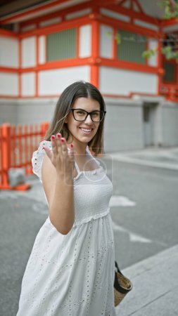 Photo for Cheerful and beautiful hispanic woman in glasses invites with friendly gesture to a japanese temple in tokyo, japan - Royalty Free Image