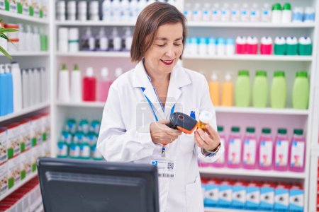 Foto de Mujer de mediana edad farmacéutico escaneo pastillas botella en la farmacia - Imagen libre de derechos