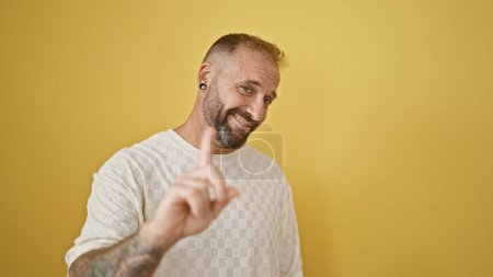 Téléchargez les photos : Joyeux jeune homme souriant avec confiance, disant non avec un doigt, debout sur un fond jaune isolé. - en image libre de droit