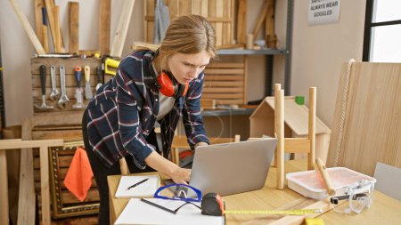 Photo for Focused woman working on laptop in a well-equipped carpentry studio - Royalty Free Image