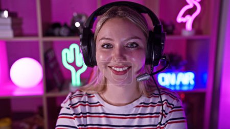 Téléchargez les photos : Jeune femme souriante avec écouteurs dans une salle de jeux dynamique éclairée par des néons - en image libre de droit