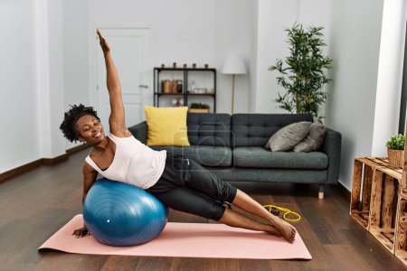 Téléchargez les photos : Afro-américaine femme entraînement abs exercice à l'aide de balle en forme à la maison - en image libre de droit