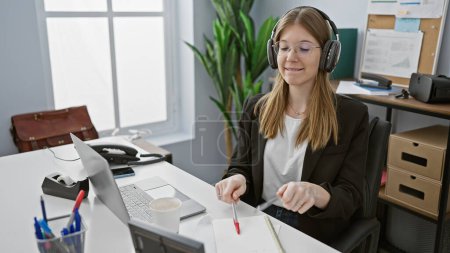 Photo for A professional young woman wearing glasses and headphones focused on her work in a modern office setting - Royalty Free Image