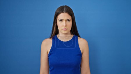 Photo for Young beautiful hispanic woman standing with serious expression over isolated blue background - Royalty Free Image