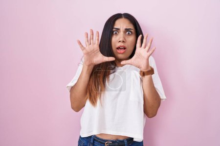 Photo for Young arab woman standing over pink background afraid and terrified with fear expression stop gesture with hands, shouting in shock. panic concept. - Royalty Free Image
