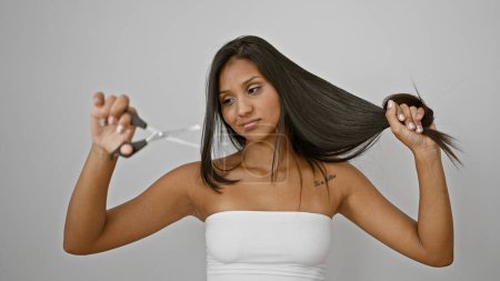 Téléchargez les photos : Jeune femme latine tenant des ciseaux et des cheveux à couper sur fond blanc isolé - en image libre de droit