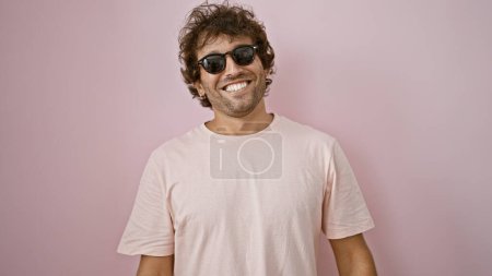 Téléchargez les photos : Jeune homme hispanique souriant portant des lunettes de soleil contre un mur rose - en image libre de droit