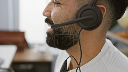 Photo for A close-up of a professional hispanic man with a beard wearing a headset in a modern office setting. - Royalty Free Image