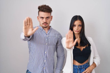 Téléchargez les photos : Young hispanic couple standing over white background doing stop sing with palm of the hand. warning expression with negative and serious gesture on the face. - en image libre de droit