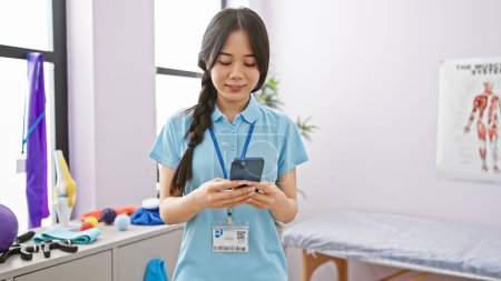 Photo for Young asian woman therapist at rehab clinic using smartphone in bright room - Royalty Free Image