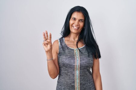 Photo for Mature hispanic woman standing over white background showing and pointing up with fingers number three while smiling confident and happy. - Royalty Free Image