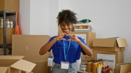 Téléchargez les photos : Femme afro-américaine bénévole faisant geste de coeur souriant au centre de charité - en image libre de droit