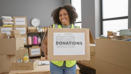 Téléchargez les photos : Femme afro-américaine avec des tresses tenant boîte de don dans un entrepôt - en image libre de droit
