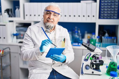 Téléchargez les photos : Homme aux cheveux gris d'âge moyen scientifique souriant confiant en utilisant le pavé tactile au laboratoire - en image libre de droit