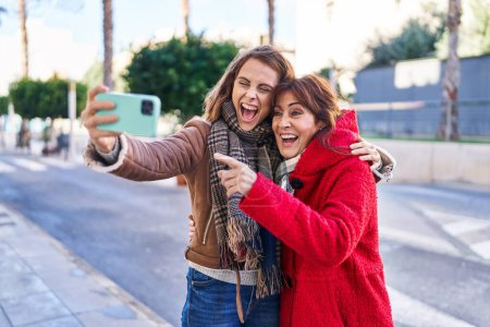 Téléchargez les photos : Two women mother and daughter make selfie by smartphone at street - en image libre de droit