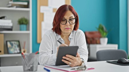 Foto de Trabajadora de negocios de mediana edad escribiendo en touchpad pensando en la oficina - Imagen libre de derechos