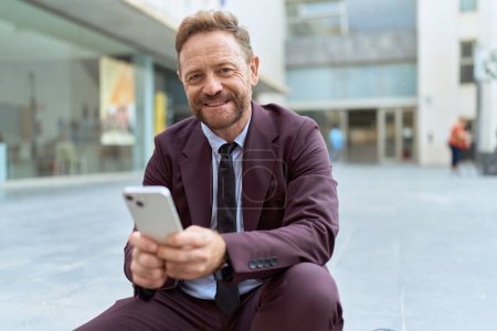 Téléchargez les photos : Homme d'âge moyen travailleur d'affaires en utilisant smartphone assis sur les escaliers à la rue - en image libre de droit