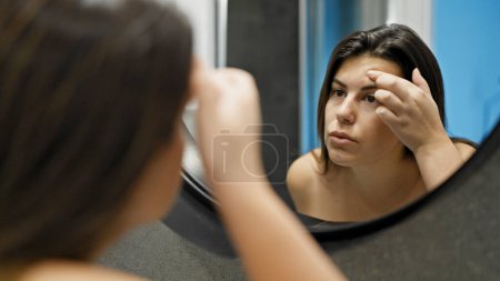Foto de Joven mujer hispana hermosa buscando granos en el espejo en el baño - Imagen libre de derechos