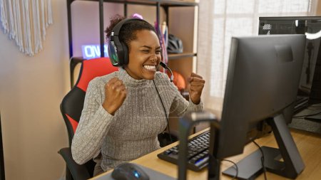 Foto de Mujer emocionada con auriculares en una sala de juegos celebra una victoria en su computadora por la noche. - Imagen libre de derechos