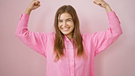Vibrant young hispanic woman flaunts her beautiful confidence, powerfully gesturing with strong arms, radiating joy and positivity, smiling cheerfully against an isolated pink background.