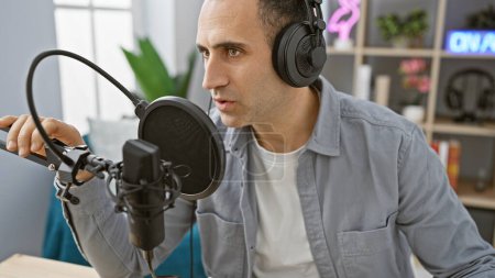 Photo for Handsome hispanic man in a studio with headphones speaking into a microphone for broadcasting or recording. - Royalty Free Image
