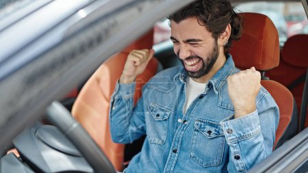 Téléchargez les photos : Jeune homme hispanique souriant voiture de conduite confiante célébrant dans la rue - en image libre de droit