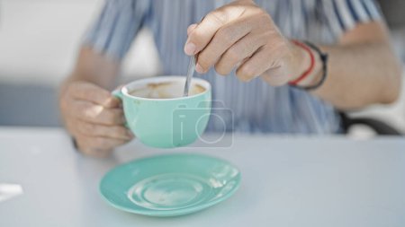 Téléchargez les photos : Gros plan d'un homme brassant du café dans une tasse turquoise sur une terrasse moderne d'un café. - en image libre de droit