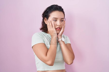 Foto de Mujer joven hispana de pie sobre fondo rosa manos cansadas cubriendo la cara, depresión y tristeza, molesto e irritado por el problema - Imagen libre de derechos