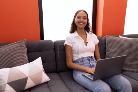 Téléchargez les photos : Jeune femme afro-américaine utilisant un ordinateur portable assis sur le canapé à la maison - en image libre de droit
