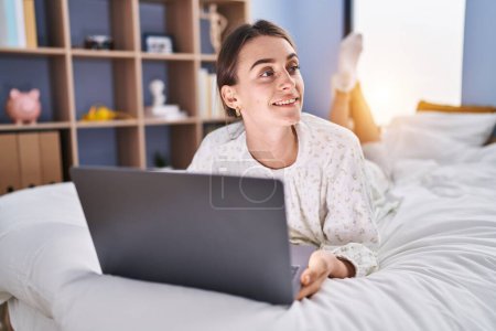 Foto de Young caucasian woman using laptop lying on bed at bedroom - Imagen libre de derechos