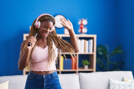 Téléchargez les photos : Femme afro-américaine écoutant de la musique chanter à la maison - en image libre de droit