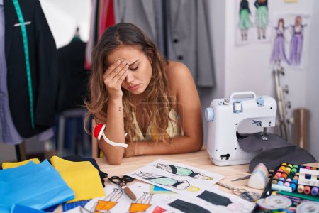 Téléchargez les photos : Young beautiful hispanic woman tailor stressed sitting on table at tailor shop - en image libre de droit