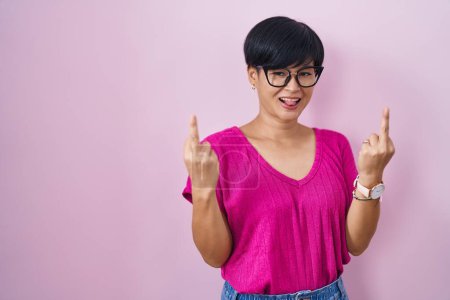 Foto de Young asian woman with short hair standing over pink background showing middle finger doing fuck you bad expression, provocation and rude attitude. screaming excited - Imagen libre de derechos