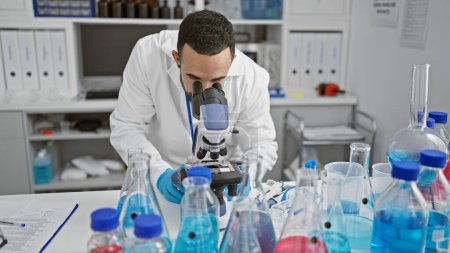 Homme hispanique en laboratoire, au microscope, entouré de matériel scientifique.