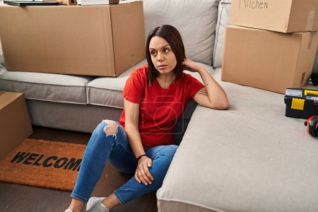 Photo for Young beautiful hispanic woman sitting on floor with tired expression at new home - Royalty Free Image