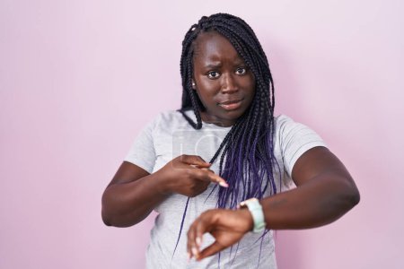 Téléchargez les photos : Jeune femme africaine debout sur fond rose pressé pointant pour regarder le temps, l'impatience, bouleversé et en colère pour retard de délai - en image libre de droit