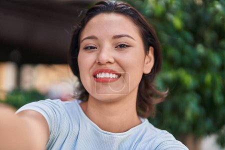 Foto de Young hispanic woman smiling confident making selfie by camera at street - Imagen libre de derechos