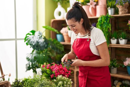 Photo for Young beautiful hispanic woman florist cutting plants at flower shop - Royalty Free Image