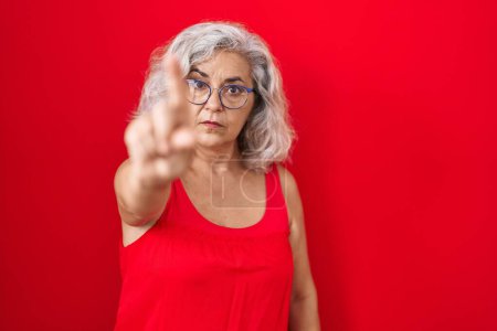 Téléchargez les photos : Femme d'âge moyen avec les cheveux gris debout sur fond rouge pointant avec le doigt vers le haut et l'expression en colère, ne montrant aucun geste - en image libre de droit