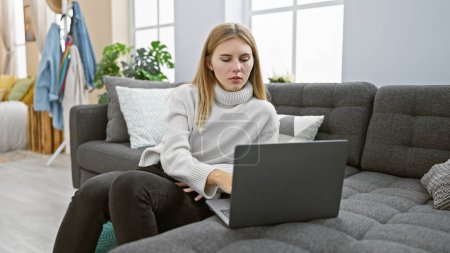 Photo for Blonde woman working on laptop in modern living room, showcasing lifestyle and interior design. - Royalty Free Image