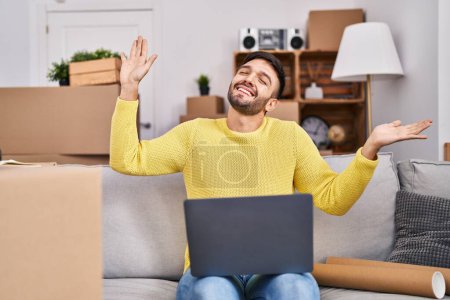 Photo for Young hispanic man using laptop stretching arms at new home - Royalty Free Image