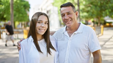 Téléchargez les photos : Père confiant partageant un câlin ensoleillé et joyeux avec sa fille souriante au parc de la ville. ensemble, ils expriment leur amour heureux et positif à l'extérieur - en image libre de droit