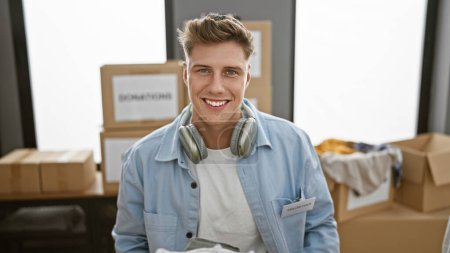 Photo for Handsome young caucasian man confidently volunteering at charity center, beaming while wearing headphones in indoor workplace - Royalty Free Image