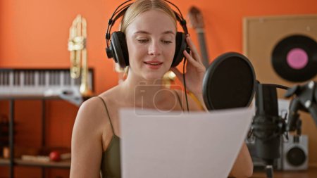 Foto de Joven mujer rubia músico sonriendo con confianza cantando canción en el estudio de música - Imagen libre de derechos