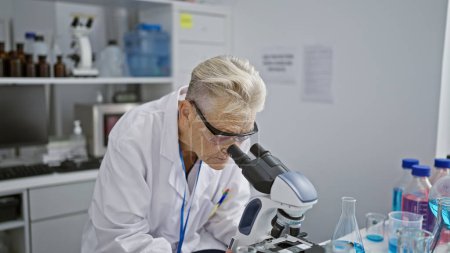 Foto de Científica senior dedicada de cabello gris inmersa en un intenso trabajo de investigación de microscopios a nivel de doctorado en laboratorio - Imagen libre de derechos