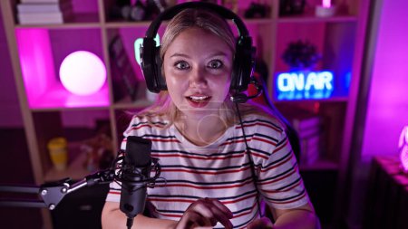 A surprised young woman wearing headphones in a neon-lit gaming room at night.