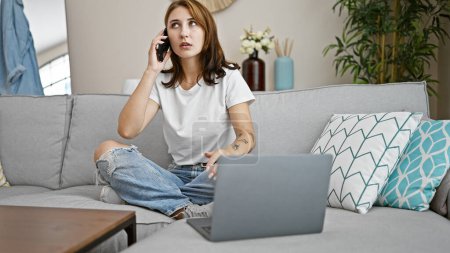 Téléchargez les photos : Jeune femme parlant sur smartphone en utilisant un ordinateur portable à la maison - en image libre de droit