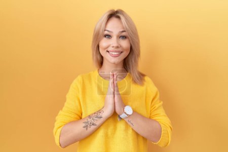 Téléchargez les photos : Jeune femme caucasienne portant un pull jaune priant avec les mains ensemble demandant pardon en souriant confiant. - en image libre de droit